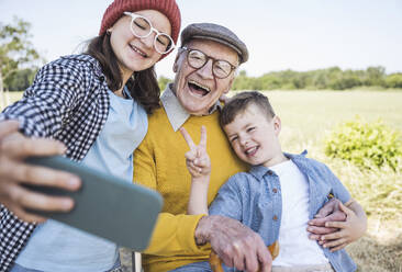 Lächelnde Geschwister und Großvater posieren für ein lustiges Familien-Selfie, aufgenommen mit einem Mobiltelefon - UUF28975