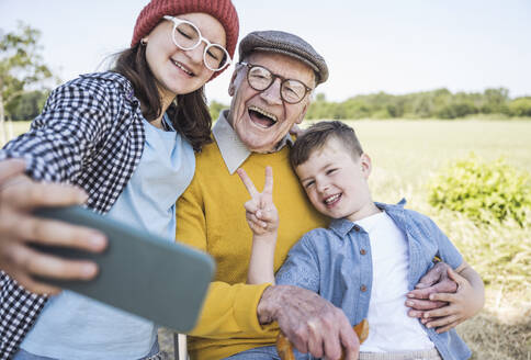 Lächelnde Geschwister und Großvater posieren für ein lustiges Familien-Selfie, aufgenommen mit einem Mobiltelefon - UUF28975