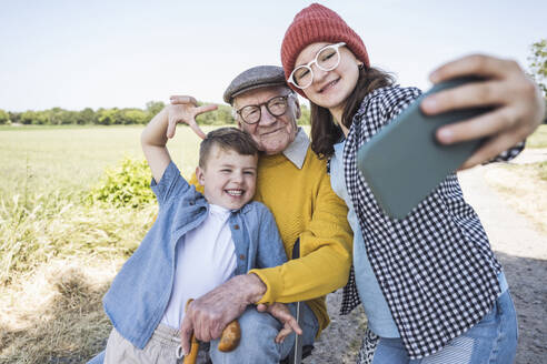 Glückliche Familie, die Erinnerungen mit einem Smartphone-Selfie festhält - Enkelin, Bruder und Großvater lächeln - UUF28976