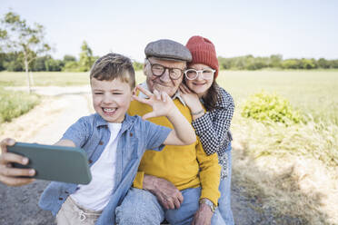 Happy boy taking selfie with sister and grandfather through smart phone - UUF28977