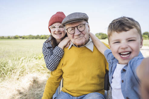 Happy boy taking selfie with sister and grandfather - UUF28978