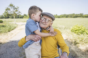 Grandson kissing grandfather on cheeks at field - UUF28981