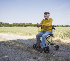 Happy senior man sitting on mobility walker - UUF28983