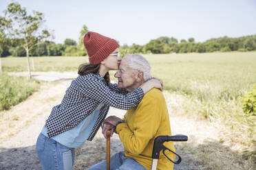 Girl wearing knit hat kissing grandfather on forehead - UUF28985