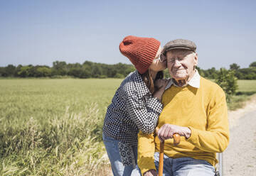 Girl wearing knit hat kissing grandfather on sunny day - UUF28987