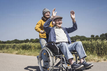 Lächelndes Mädchen mit Großvater, der im Rollstuhl sitzt und Musik hört - UUF28994