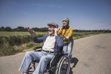 Glückliches Mädchen mit Großvater im Rollstuhl sitzend und Musik hörend auf der Straße - UUF28997