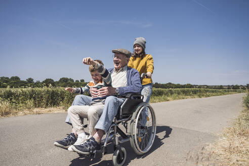 Glückliches Mädchen mit Großvater und Enkel im Rollstuhl sitzend auf der Straße - UUF29001