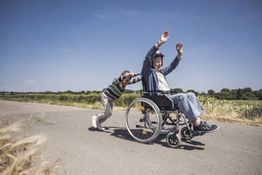 Junge schiebt Rollstuhl mit älterem Mann an einem sonnigen Tag - UUF29005