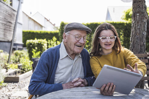 Lächelndes Mädchen, das seinem Großvater im Hinterhof einen Tablet-PC beibringt - UUF29011