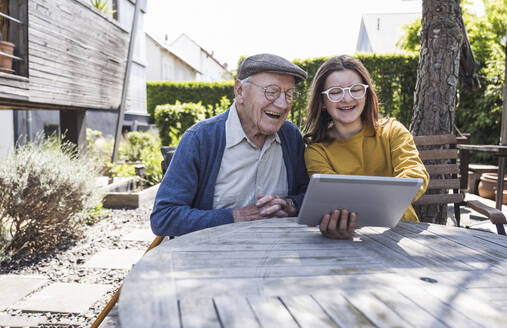 Glückliches Mädchen, das seinem Großvater im Hinterhof einen Tablet-PC beibringt - UUF29012