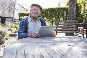 Lächelnder älterer Mann sitzt mit Tablet-PC am Tisch - UUF29017