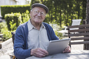 Smiling senior man sitting with tablet PC at table in back yard - UUF29018