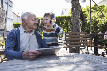 Lächelnder älterer Mann mit Enkel, der drahtlose Kopfhörer trägt - UUF29023