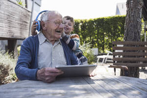 Glücklicher älterer Mann mit Enkel, der drahtlose Kopfhörer einstellt - UUF29024