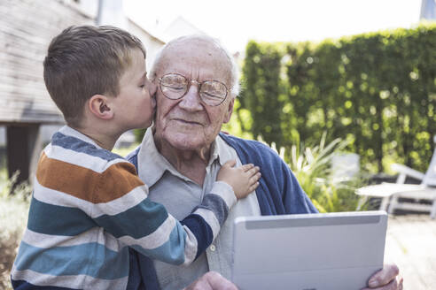 Boy kissing and embracing grandfather holding tablet PC - UUF29027