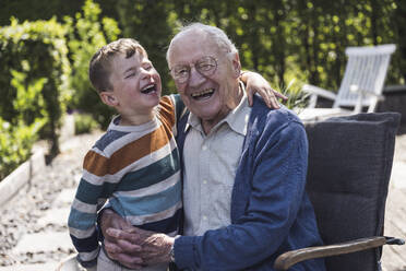 Cheerful boy with grandfather sitting in armchair - UUF29028