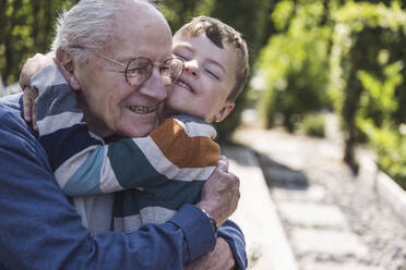Happy boy hugging grandfather in back yard - UUF29029