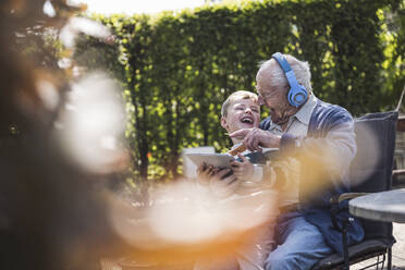 Fröhlicher älterer Mann mit drahtlosen Kopfhörern, der mit seinem Enkel Spaß hat - UUF29031