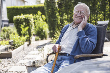 Lächelnder älterer Mann mit Gehstock im Sessel sitzend - UUF29035