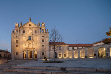 Exterior of ancient historical church with ornamental elements and cross on top located on paved street under cloudless evening sky in Avila - ADSF44339