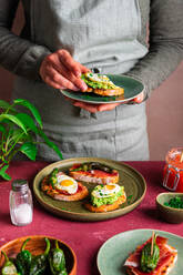 Unrecognizable chef in apron putting appetizing vegetarian toast with avocado and fried egg on round plate while serving healthy meal for breakfast - ADSF44347