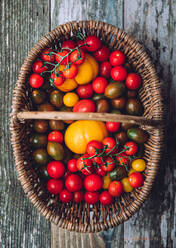 Top view of wicker basket filled with ripe fresh colorful tomatoes placed on wooden table - ADSF44352