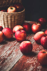 Wicker basket filled with fresh ripe red apples placed on shabby timber cupboard against wooden wall in countryside house during harvest season - ADSF44356