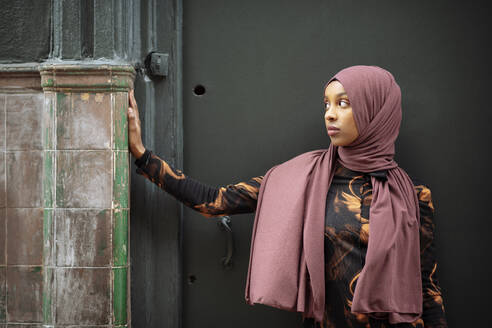 Young woman in hijab leaning against tiled wall - ISF26140