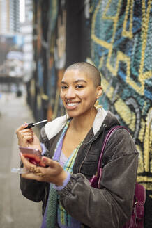 Portrait of hipster young woman applying lip gloss in street - ISF26142