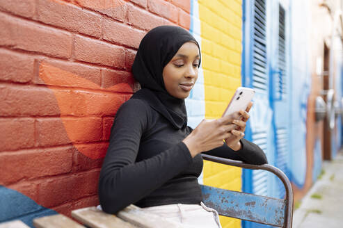 Young woman wearing hijab using phone in street - ISF26149