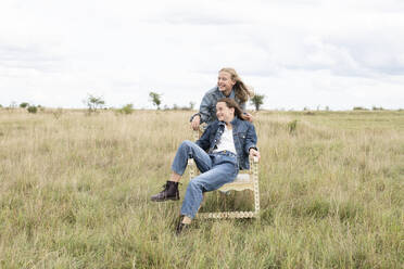 Smiling girl friends (10-11) sitting in chair in field - ISF26156