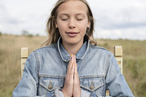 Girl (10-11) in denim jacket meditating outdoors - ISF26164