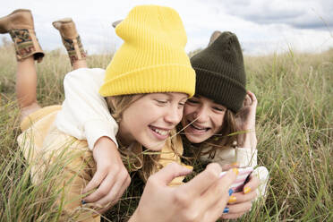 Smiling girl friends (10-11) lying in grass and using phone - ISF26199