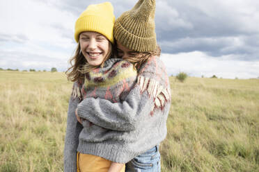 Smiling girl friends (10-11) wearing one sweater in field and hugging - ISF26207