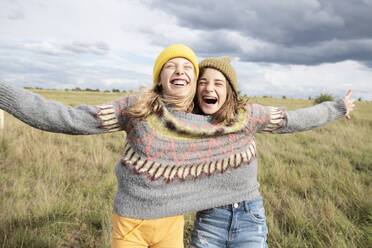 Smiling girl friends (10-11) wearing one sweater in field - ISF26208