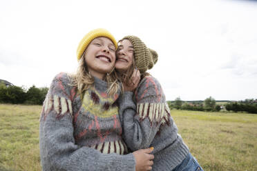 Smiling girl friends (10-11) wearing one sweater in field - ISF26210