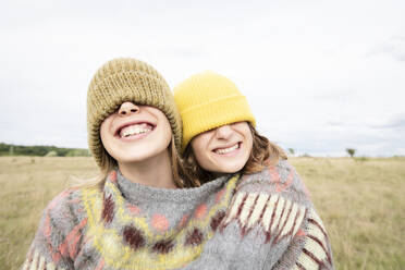 Smiling girl friends (10-11) wearing beanies over eyes - ISF26214