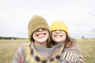 Smiling girl friends (10-11) wearing beanies over eyes - ISF26215