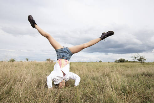 Smiling girl (10-11) standing on head in field - ISF26220