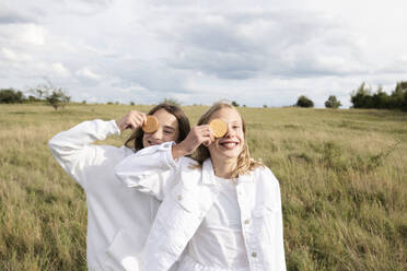 Smiling girl friends (10-11) holding in front of eyes - ISF26224