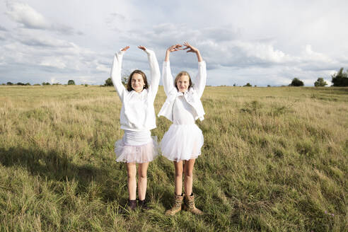 Smiling girl friends (10-11) doing ballet pose in field - ISF26230