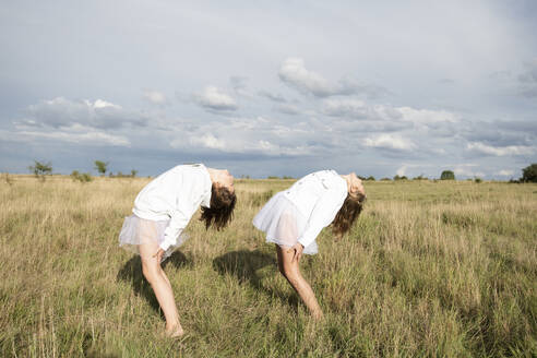 Smiling girl friends (10-11) doing ballet pose in field - ISF26232