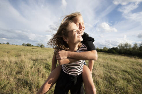 Smiling girl (10-11) giving friend piggyback ride - ISF26234