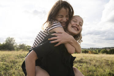 Smiling girl (10-11) giving friend piggyback ride - ISF26236