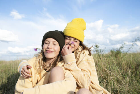 Smiling girl friends (10-11) holding flowers and sitting in grass - ISF26245