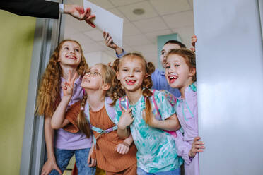 Hand eines Lehrers, der Schulkindern in der Klassenzimmertür stehend ein Zeugnis ausstellt - MDOF01394