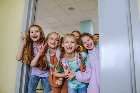 Fröhliche Schulkinder stehen gestikulierend in der Tür eines Klassenzimmers - MDOF01397