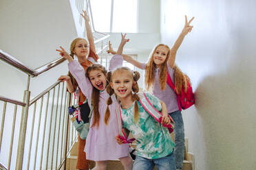 Smiling schoolgirls with hand raised standing on school staircase - MDOF01399