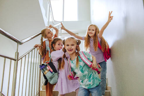 Glückliche Schulmädchen mit erhobener Hand auf der Schultreppe stehend - MDOF01400